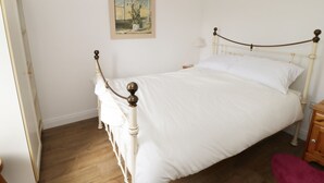 A bedroom with a white bed, wooden headboard, and a painting on the wall. - The Hen House (Thornton-Cleveleys)