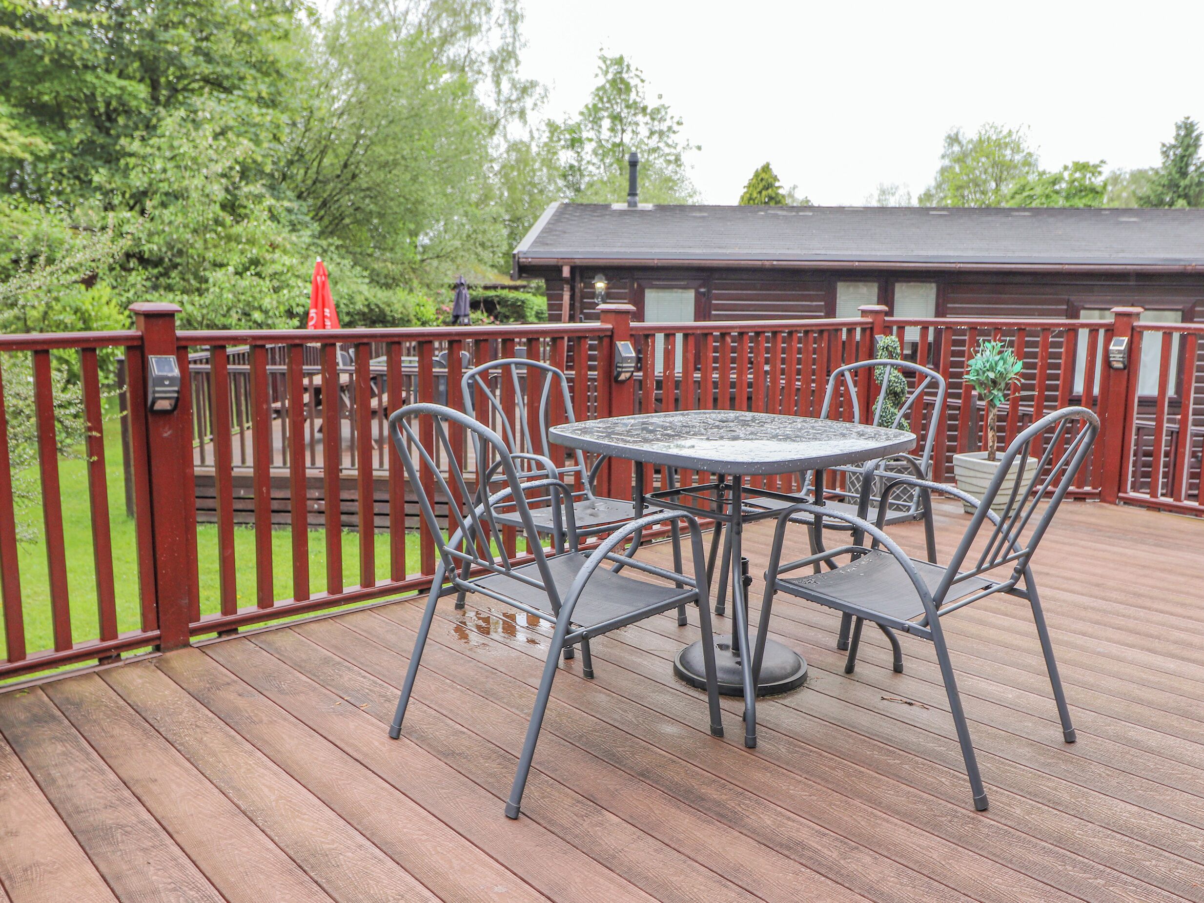 Eine Holzterrasse mit einem Metalltisch und -stühlen, umgeben von einem roten Geländer.