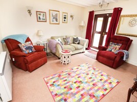 Una sala de estar acogedora con dos sillones rojos, un sofá beige y una alfombra con motivos coloridos.