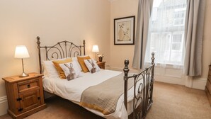 A neatly arranged bedroom with a metal bed frame, a wooden nightstand with a lamp, and a window with curtains. - Flat 4 (Whitby)
