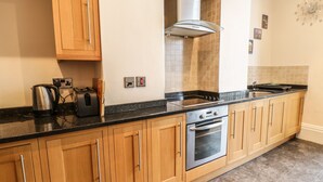 A kitchen with wooden cabinets, a stainless steel range hood, a built-in oven, and a black countertop. - Flat 4 (Whitby)