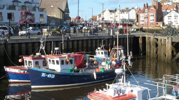 A harbor with boats docked, a pier with people, and buildings in the background. - Flat 4 (Whitby)