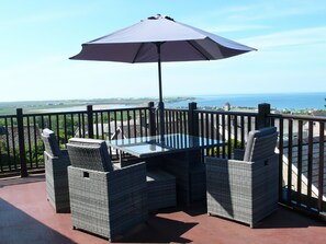 A balcony with wicker furniture, a glass table, and a large umbrella. - Maesawel Studio (Harlech)