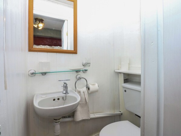 A small bathroom with a white sink, a mirror, a toilet, and a glass shelf. - Maesawel Studio (Harlech)