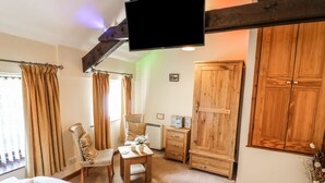 A room with a bed, a chair, a small table, a wooden wardrobe, and a television mounted on the ceiling. - Juniper Cottage (Ambleside)