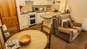 A compact kitchen with white cabinets, a dining table with chairs, and a sofa. - Juniper Cottage (Ambleside)