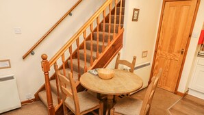 A wooden staircase with a carpeted floor, a round wooden table with chairs, and a door with a red handle. - Juniper Cottage (Ambleside)