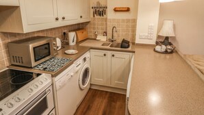 A compact kitchen with a microwave, toaster, oven, and washing machine. - Juniper Cottage (Ambleside)