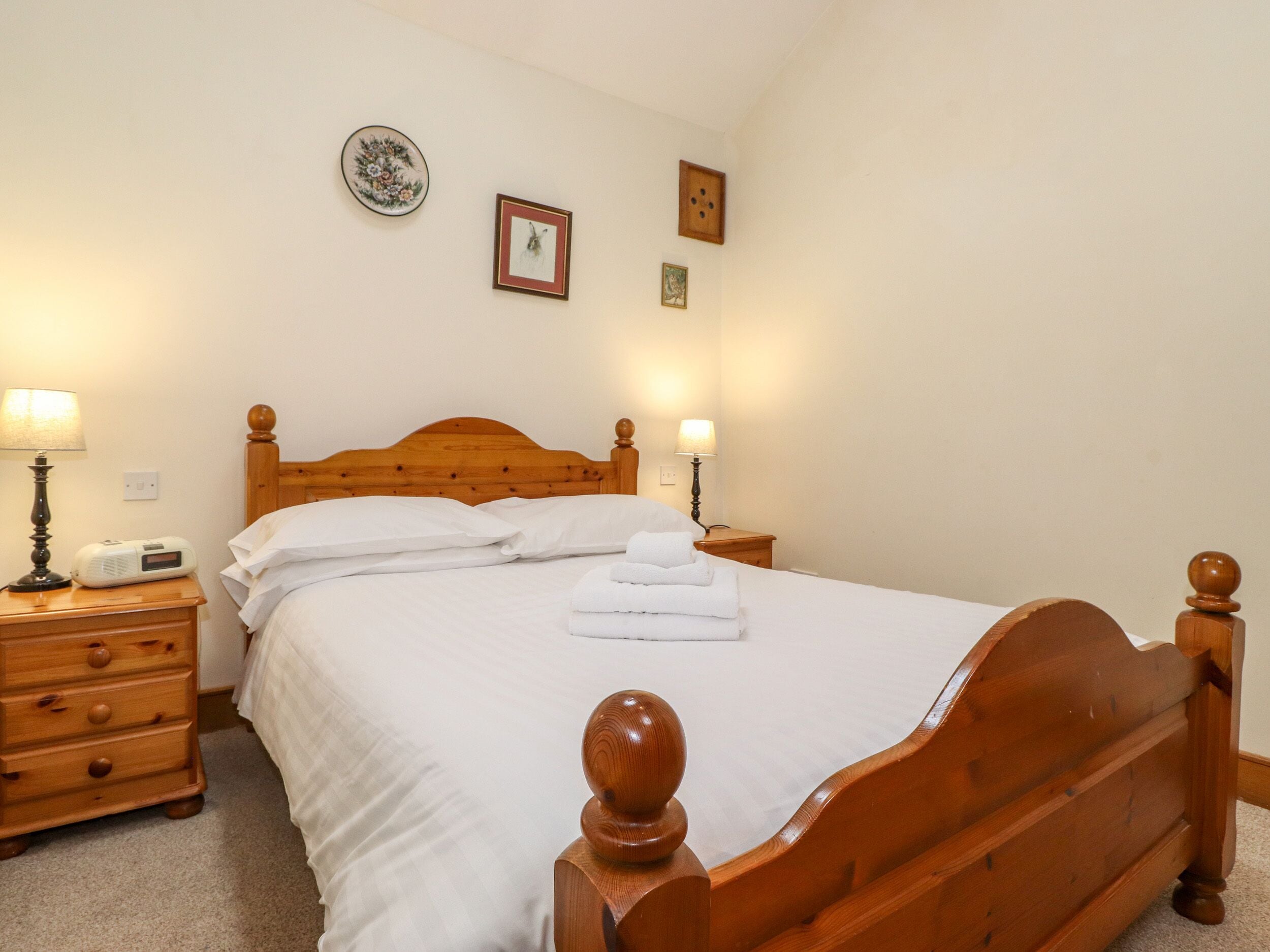 A neatly made bed with white linens and a wooden headboard, flanked by two bedside tables with lamps and a radio.