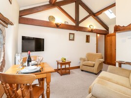 A dining area with a wooden table set for two, a sofa, and a television mounted on the wall.