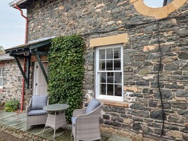 A stone building with a window and a door, ivy-covered wall, and two wicker chairs with cushions.