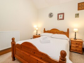 A neatly made bed with white linens, two bedside tables with lamps, a wooden headboard, and a radiator.