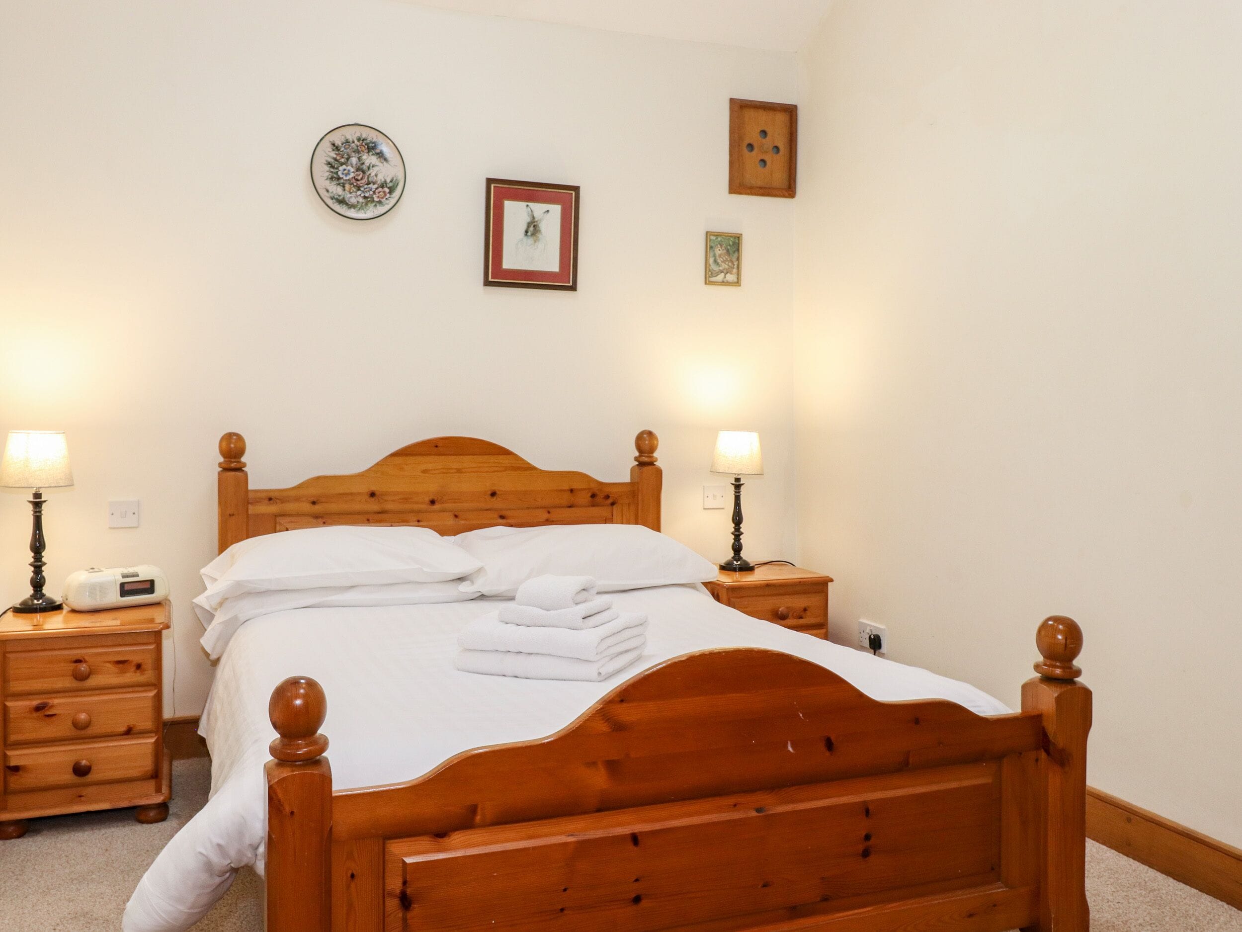 A neatly made bed with white linens and towels, wooden headboard, bedside tables with lamps, and framed pictures on the wall.