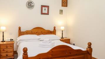 A neatly made bed with white linens and towels, wooden headboard, bedside tables with lamps, and framed pictures on the wall.