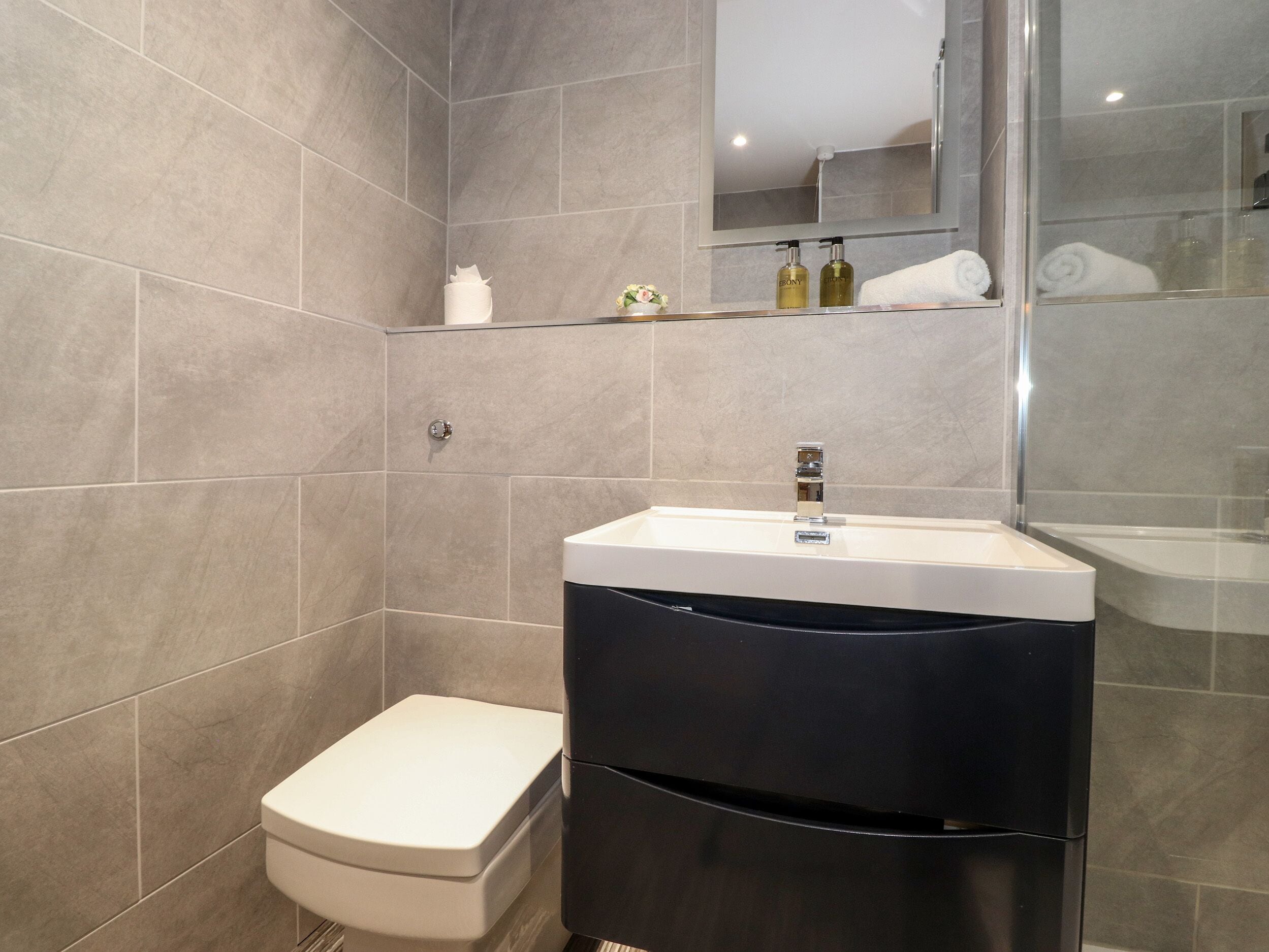 A modern bathroom with a toilet, a sink with a mirror, and toiletries on a shelf.