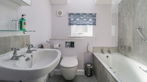 Une salle de bain moderne dotée d’un puits de lumière, d’une baignoire sur pieds, d’un lavabo et de toilettes.
