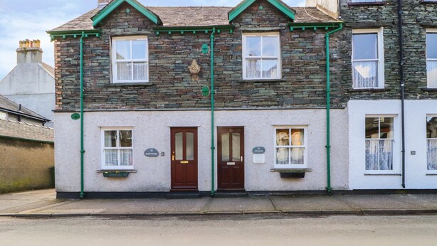 Une maison en pierre à deux étages, avec une porte d’entrée marron, deux fenêtres au rez-de-chaussée et un petit porche.