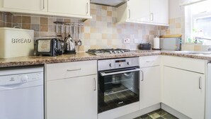 Une cuisine moderne avec des meubles blancs, une cuisinière à gaz, un four encastré, un garde-pain et une machine à café.