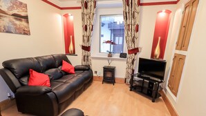 A living room with a black leather sofa, a television, a small table with a vase, and a window with curtains. - Granary Nook (Windermere)