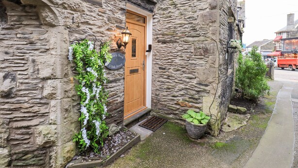 A stone building with a wooden door, a sign for Granary Nook, and a small garden area with plants. - Granary Nook (Windermere)