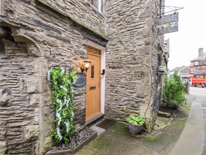 A stone building with a wooden door, a sign for Granary Nook, and a small garden area with plants. - Granary Nook (Windermere)