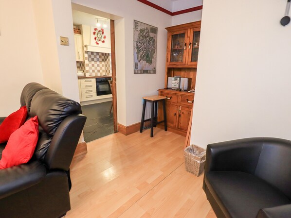 A living room with a black leather sofa, a wooden cabinet, and a kitchen area with a microwave and a small table. - Granary Nook (Windermere)