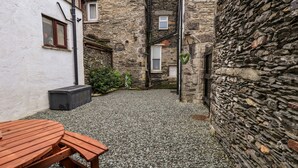A courtyard with stone walls, a wooden bench, and a small table. - Granary Nook (Windermere)
