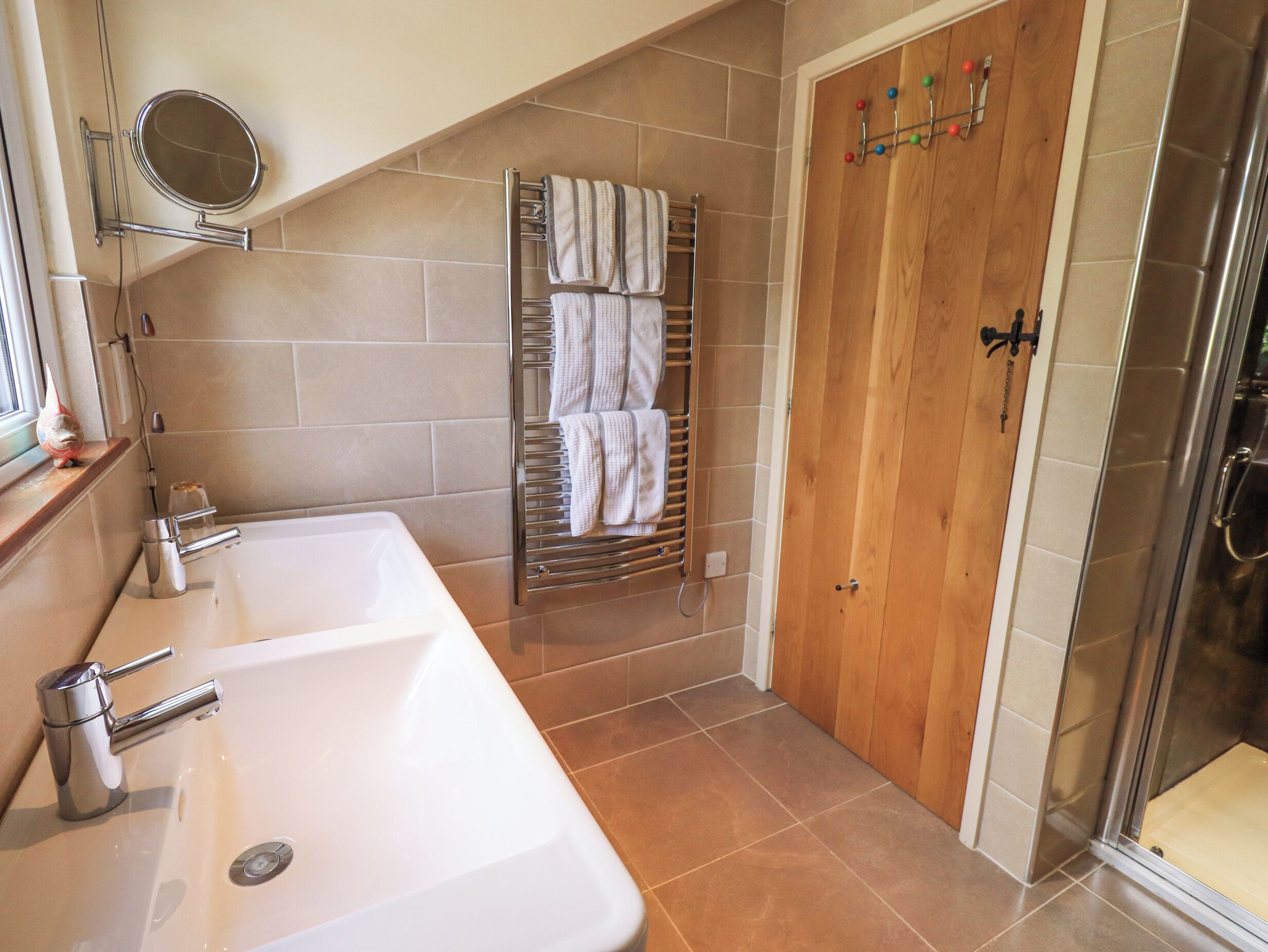 A bathroom with a double sink, a towel rack, a wooden door, and a shower area.