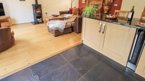 A modern living room with a fireplace, a dining area with a kitchen counter, and a red accent wall. - Stonegarth Mews (Ambleside)