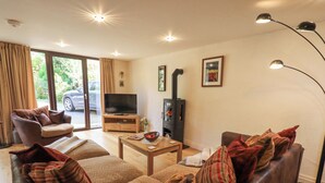 A living room with a sofa, a coffee table, a TV, and a fireplace. - Stonegarth Mews (Ambleside)