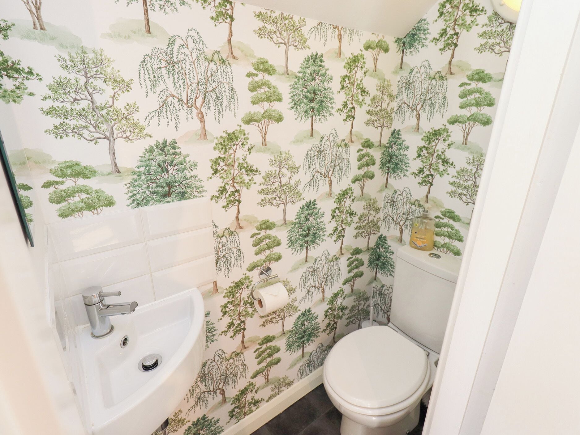 A bathroom with a sink, toilet, and a wall with a tree pattern.