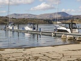 Uma marina com barcos atracados, águas calmas e montanhas ao fundo.