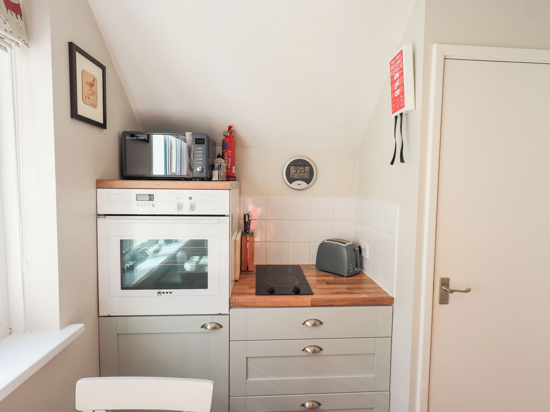 Een kleine keuken met een magnetron, oven, broodrooster en een klok aan de muur.