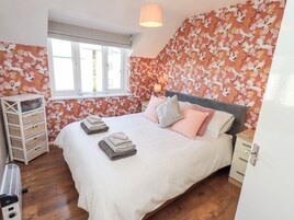 Quarto com cama, almofadas, mesa de cabeceira, abajur, janela e parede com padrão floral.