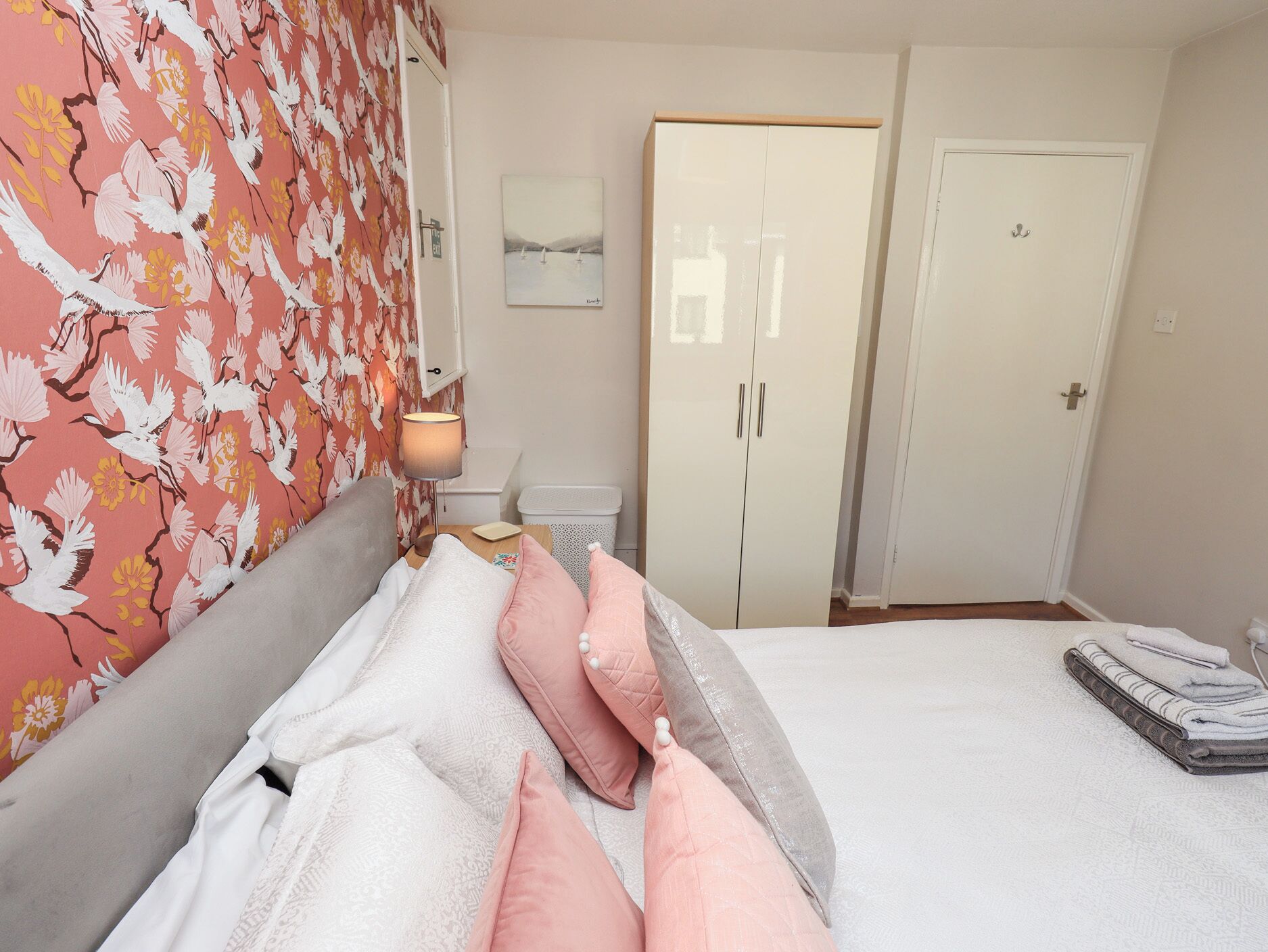 A hotel room with a bed, a bedside table, a lamp, a wardrobe, and a door.