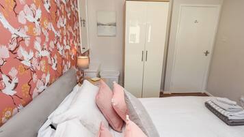 A hotel room with a bed, a bedside table, a lamp, a wardrobe, and a door.