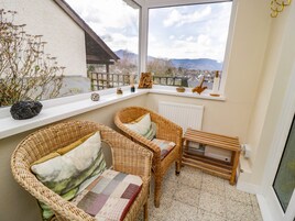A cozy balcony with wicker furniture, a view of a cityscape, and a small table with decorative items.