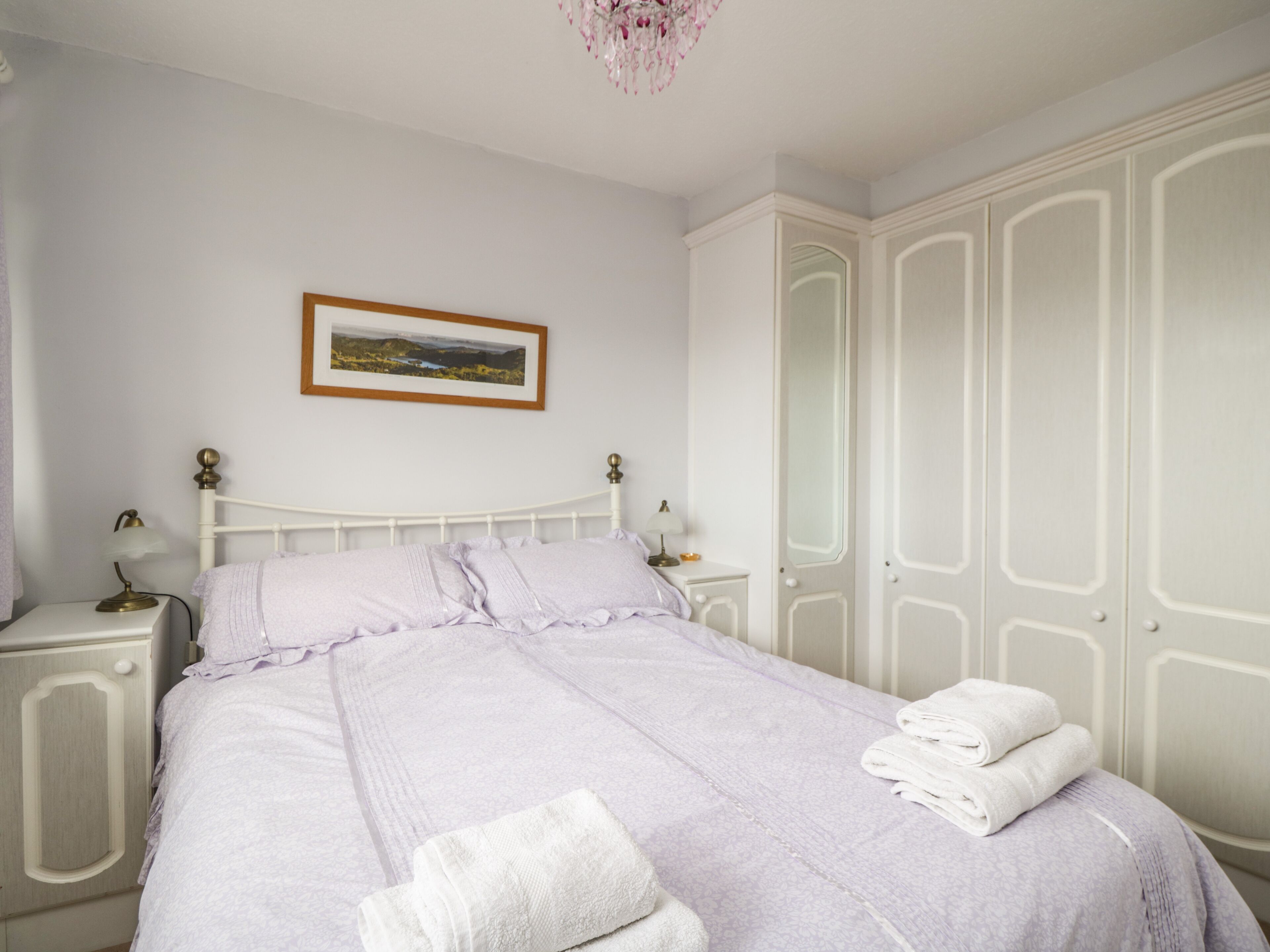 A neatly made bed with a white headboard, a bedside table with a lamp, and a wardrobe with mirrored doors.