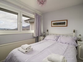 A bedroom with a bed, a window with a view of the outdoors, a radiator, and a bedside table with a lamp.