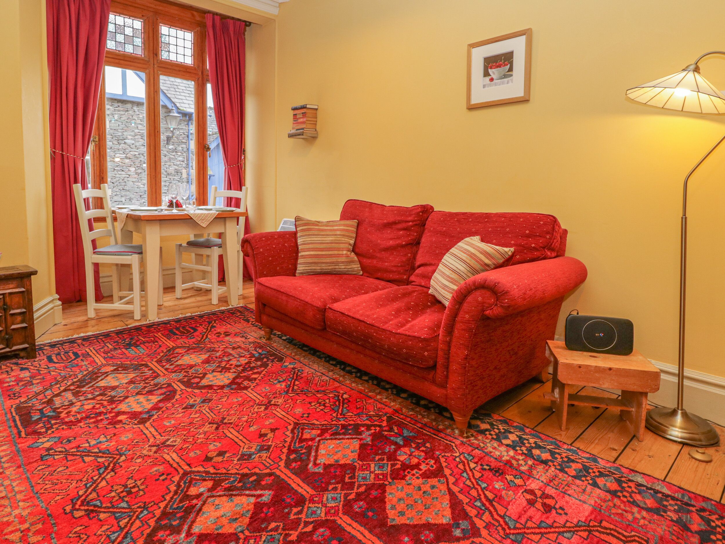 A cozy living room with a red sofa, a patterned rug, a small table, and a lamp.