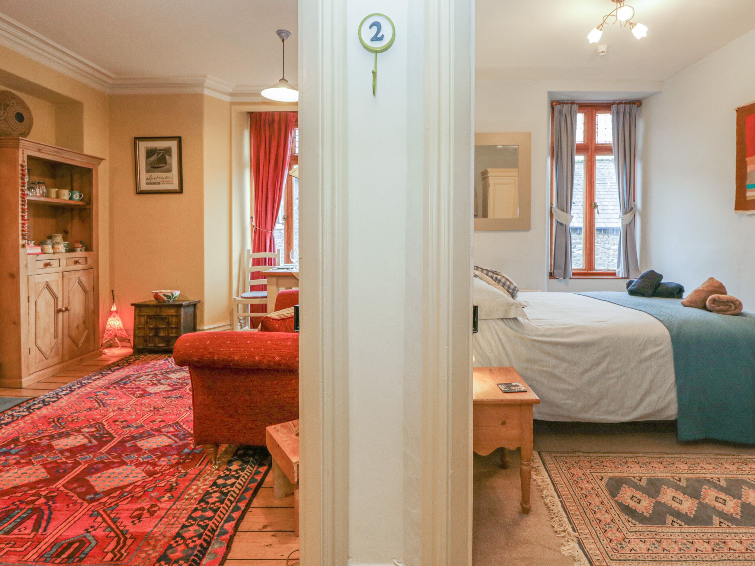 Une chambre confortable avec un lit, un bureau et une chaise. Il y a une fenêtre avec des rideaux, un tapis rouge et un meuble en bois.