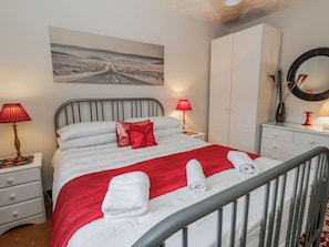 A neatly arranged bedroom with a bed, two bedside tables, a wardrobe, a mirror, and a painting on the wall.