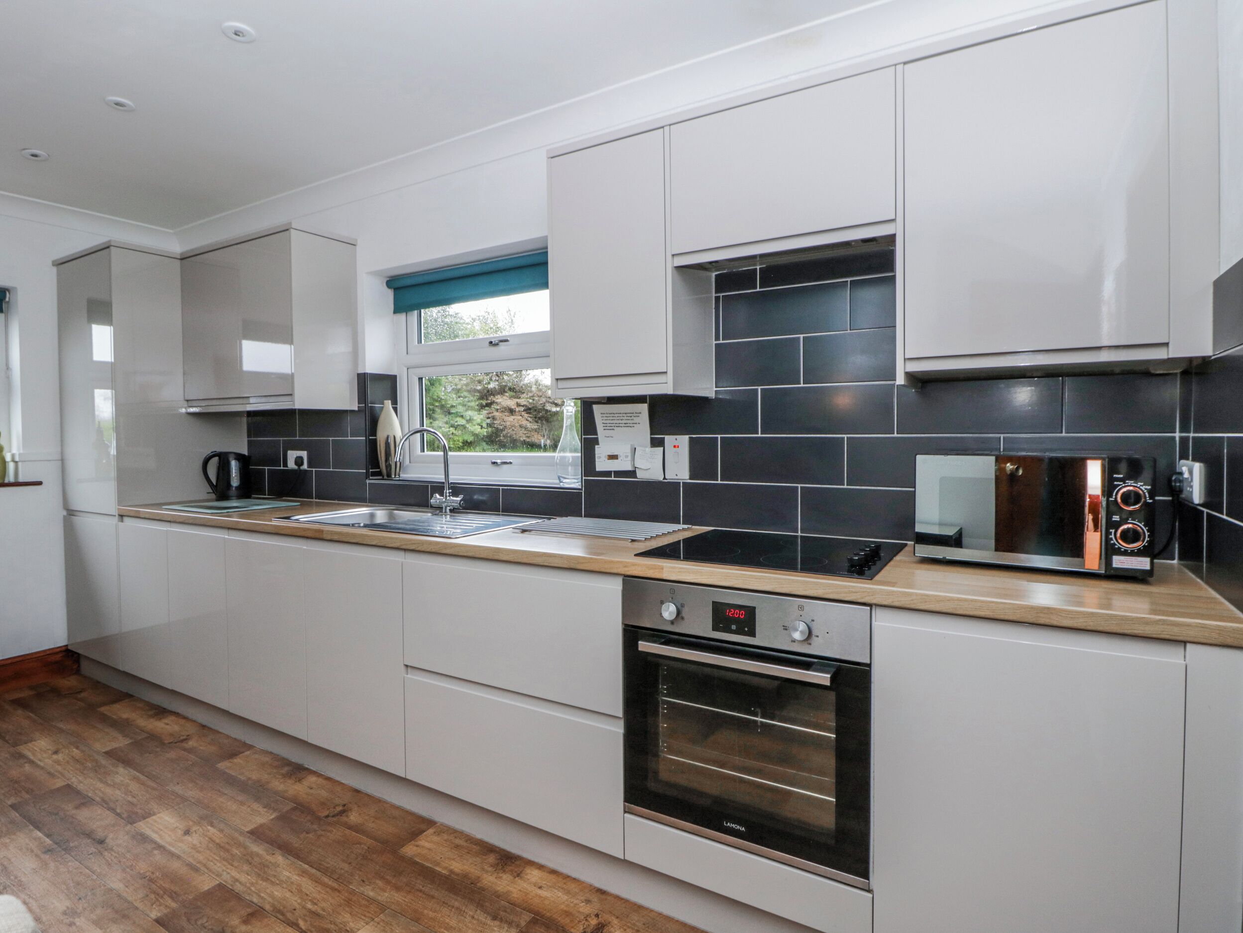 A modern kitchen with a built-in oven, a stovetop, a sink, and a window with a view of greenery outside.