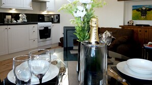 A modern kitchen with white cabinets, a black countertop, and a dining area with a table set for two. - Daisy Cottage (Penrith)