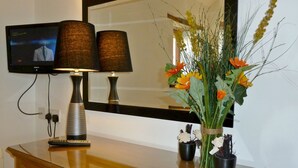 A room with a wooden dresser, a flat-screen TV mounted on the wall, two lamps, and a vase with flowers. - Daisy Cottage (Penrith)