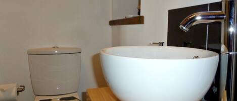 A bathroom with a toilet, a white sink, and a chrome faucet.