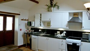 A kitchen with white cabinets, a stove, a dishwasher, and a microwave. - Daisy Cottage (Penrith)