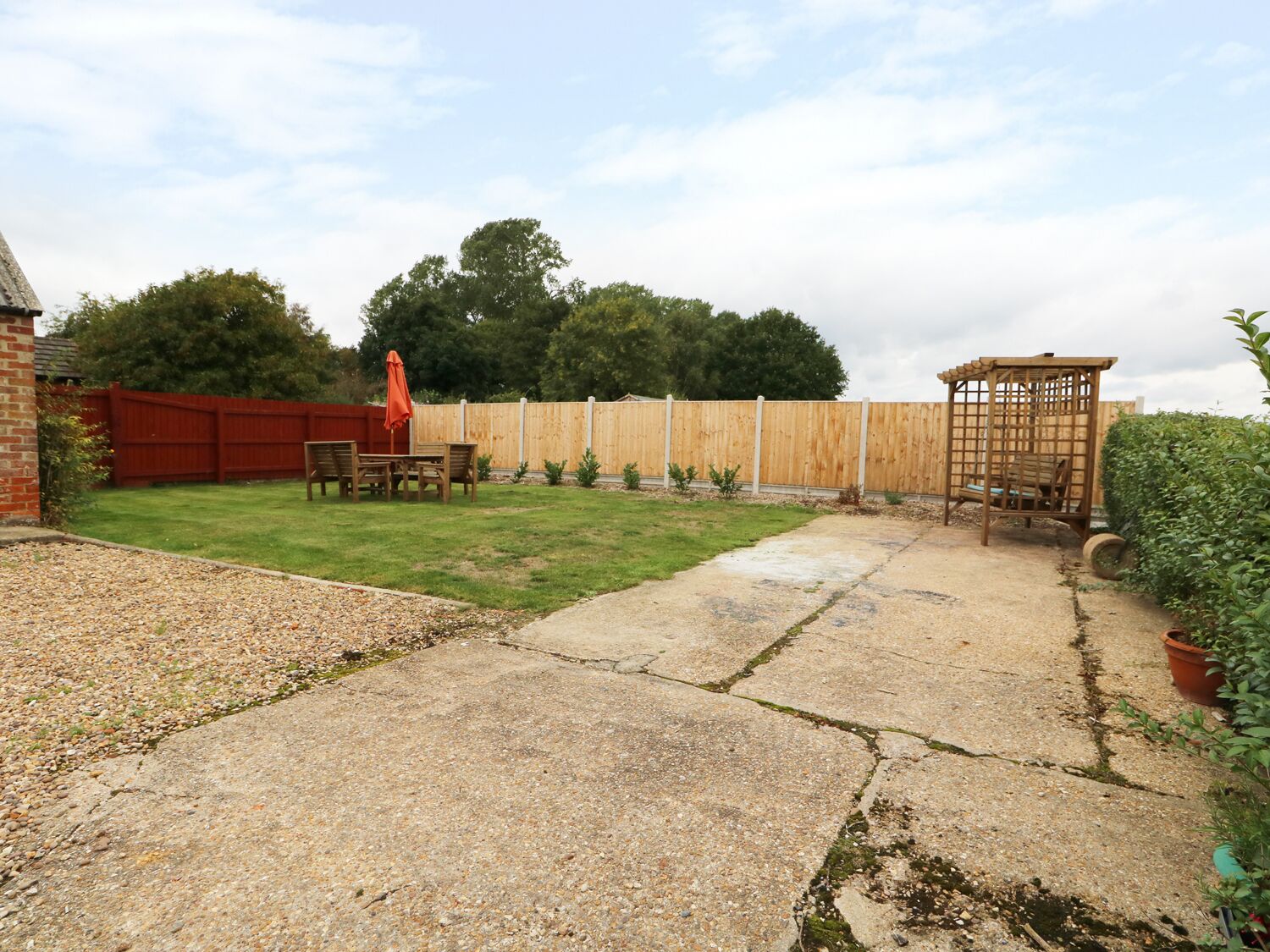 Un jardin à l’arrière de la maison, avec une terrasse, une clôture en bois et un petit espace aménagé en jardin.