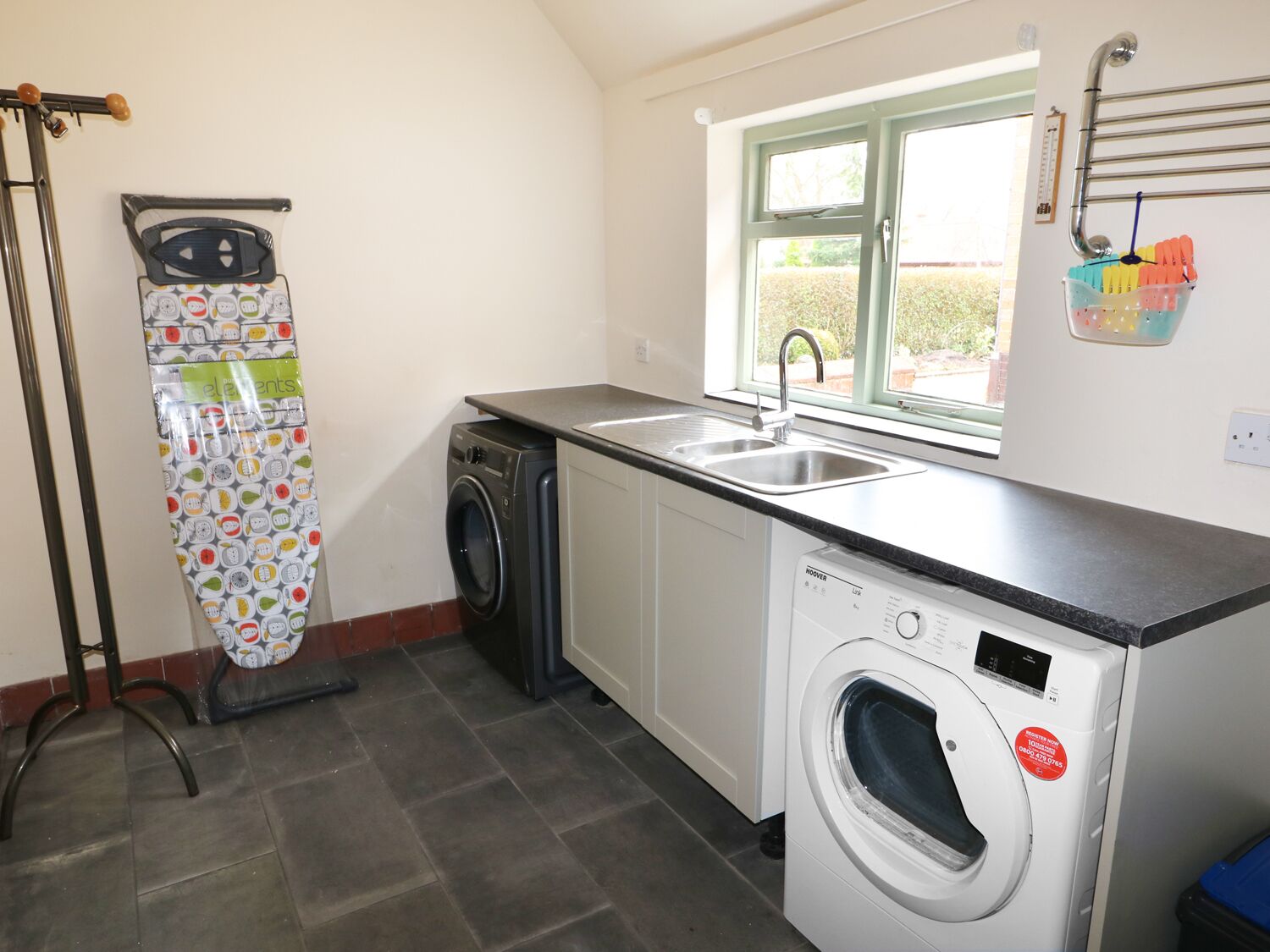 A compact kitchen with a washing machine, a drying rack, and a window with a view of greenery.