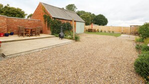 Une terrasse en gravier avec un bâtiment en briques, un barbecue et des meubles d’extérieur.